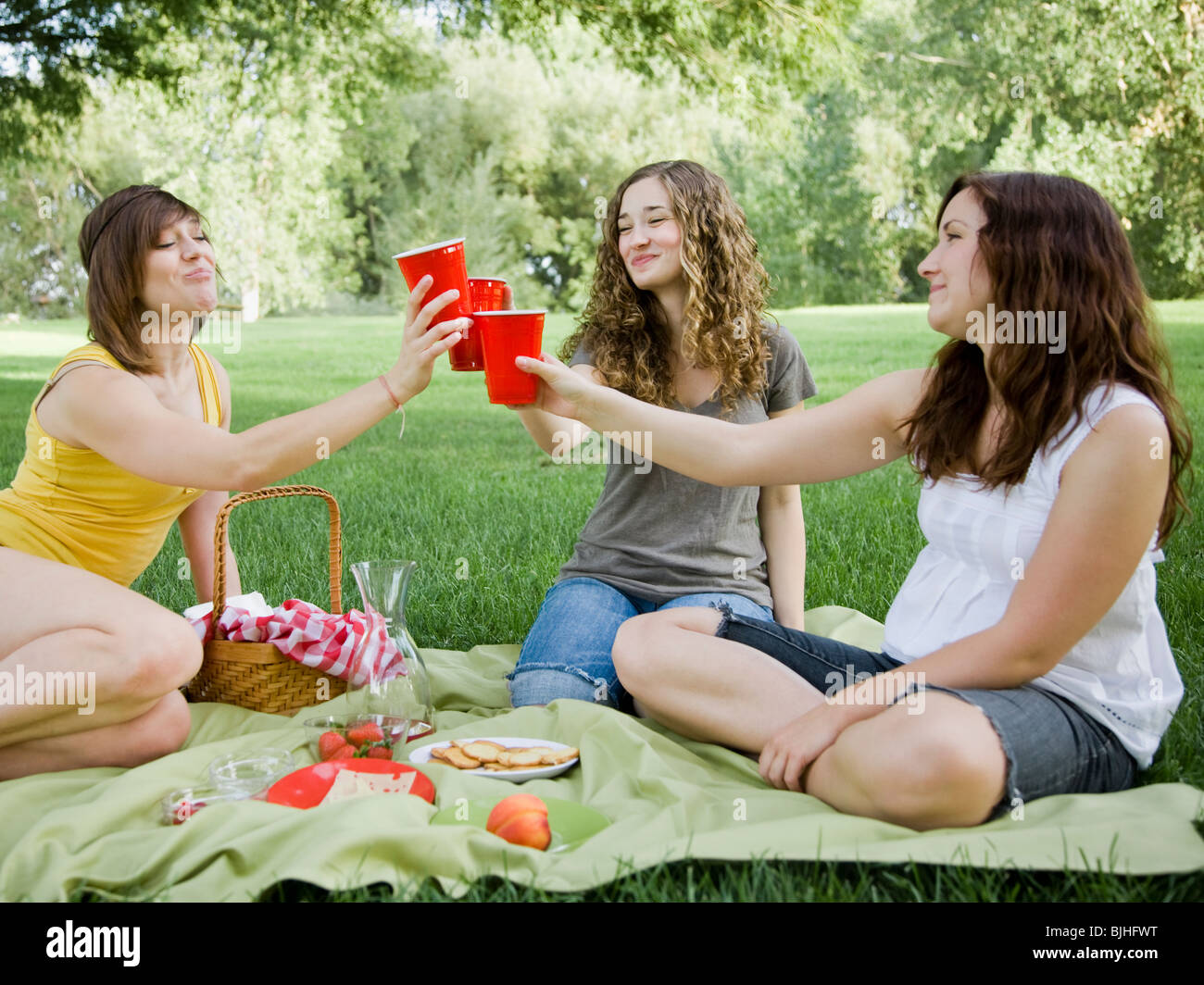 three young women having a picnic on the grass in a park Stock Photo