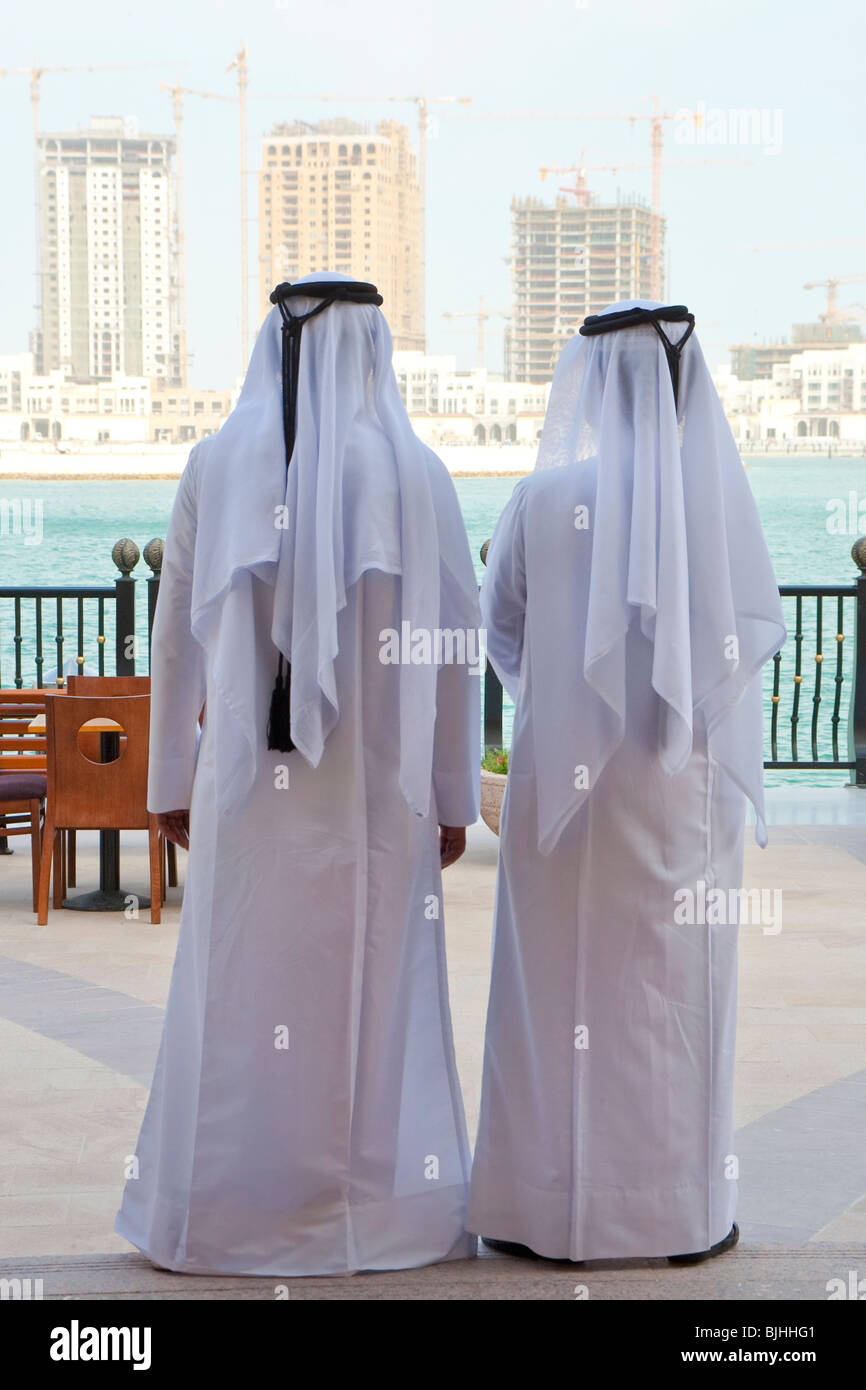 Two anonymous Arab men in traditional white clothing looking at the  construction of new modern skyscrapers on the horizon Stock Photo - Alamy
