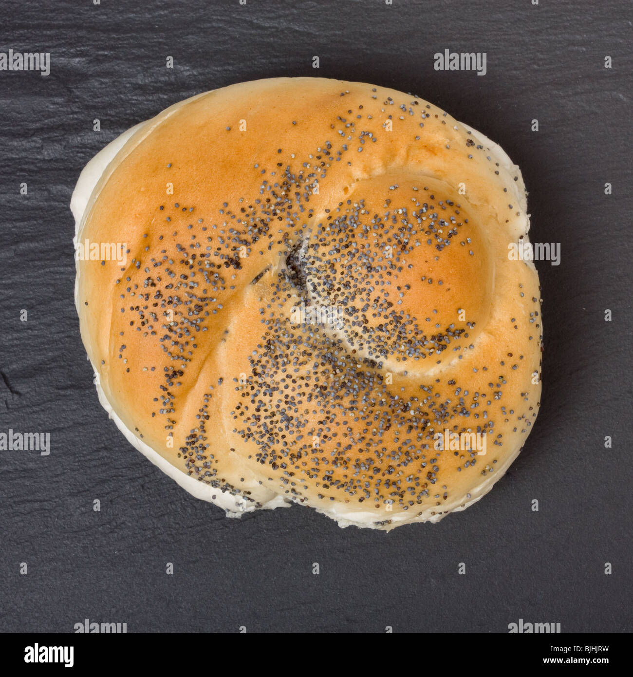 Seeded bread roll from high viewpoint against dark slate background. Stock Photo