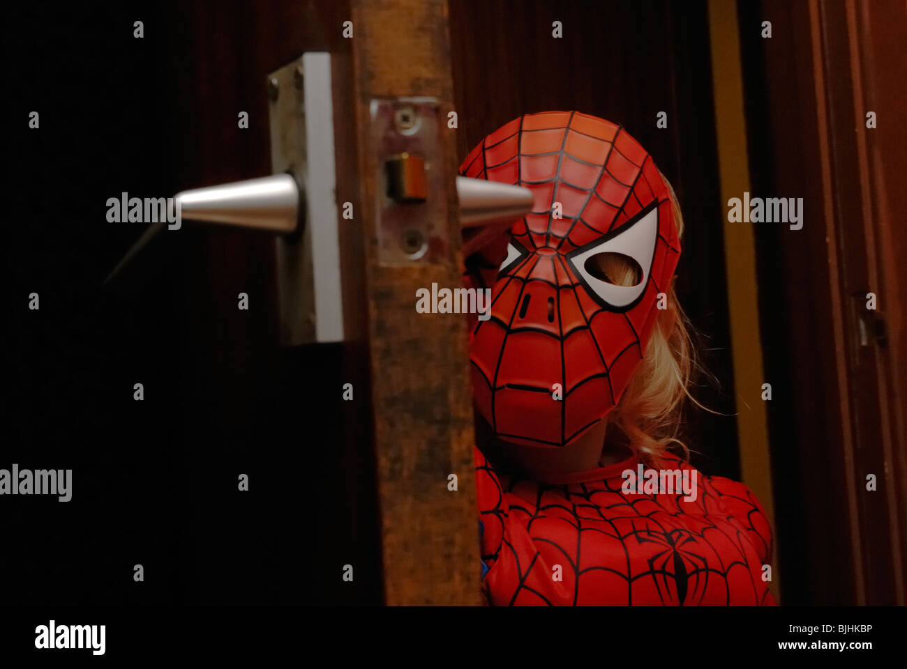 Young girl peeking round a door wearing a Spiderman costume, Wales. Stock Photo