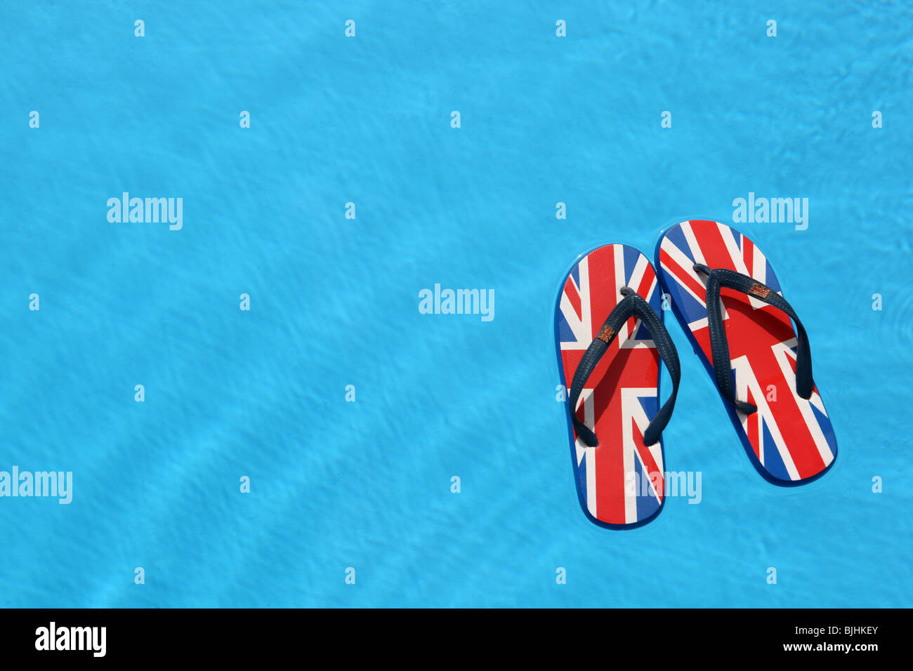 A pair of unbranded flip flops that have been printed with the British Union Jack flag floating on a swimming pool water surface Stock Photo