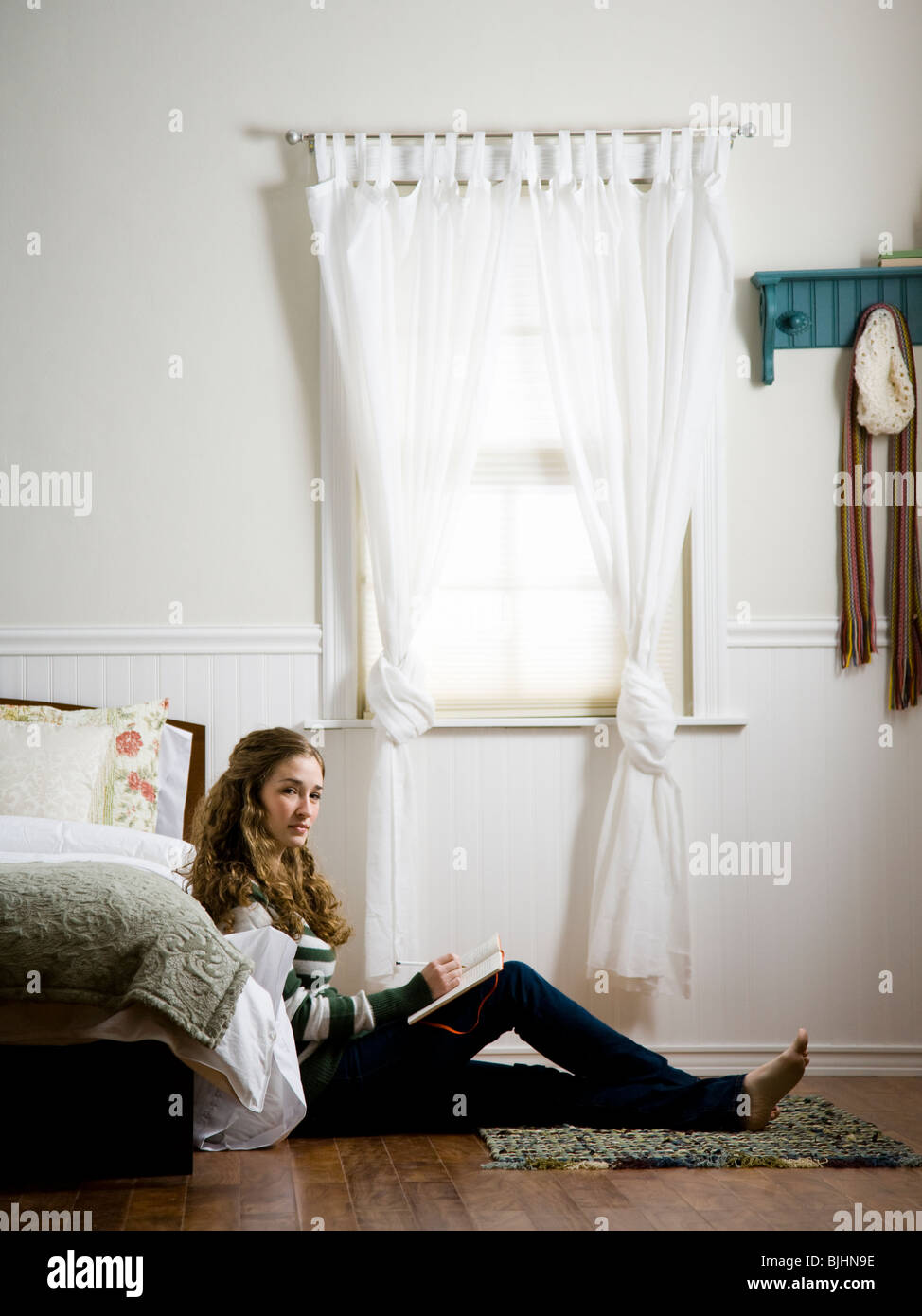 woman sitting on the floor of her bedroom writing in a journal Stock