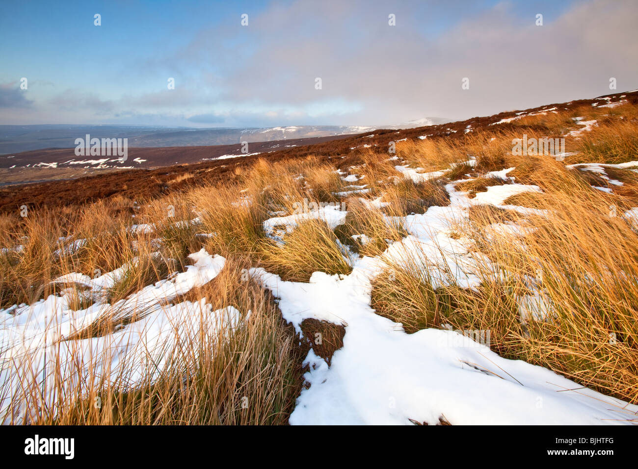 Warm afternoon light hits the slopes and the remainder of some Winter snow on the slopes of Bleaklow in The Peak District Stock Photo