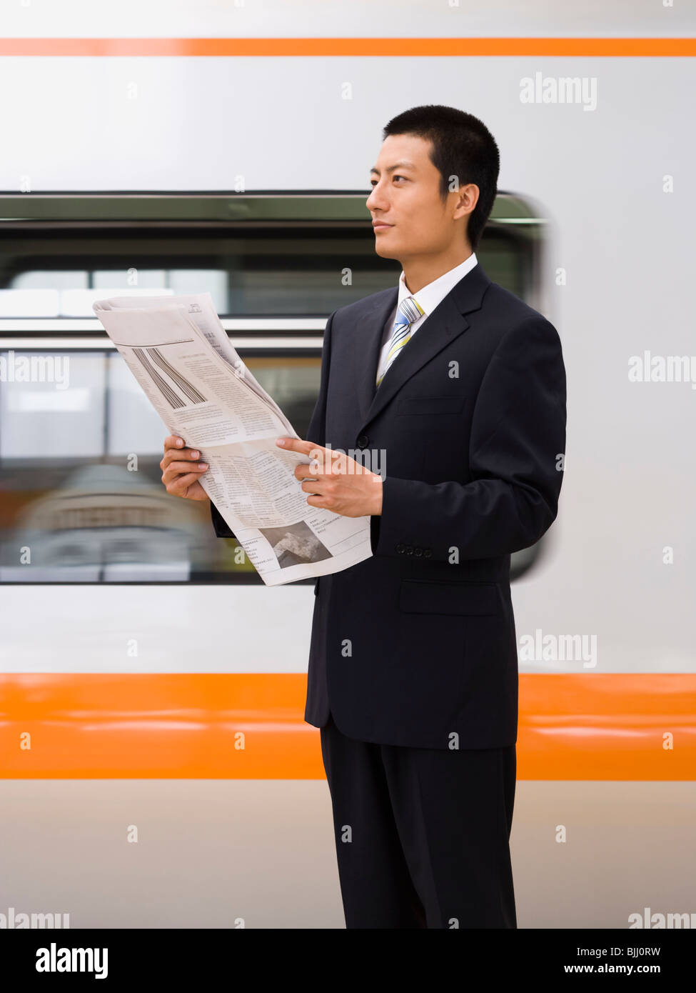 Businessman reading newspaper with subway in background Stock Photo