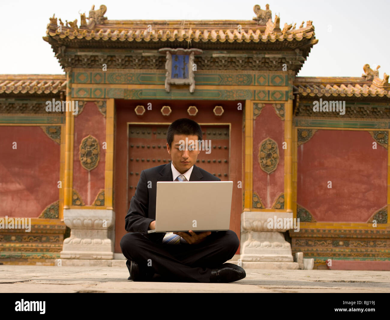 Businessman sitting cross legged outdoors with laptop Stock Photo - Alamy