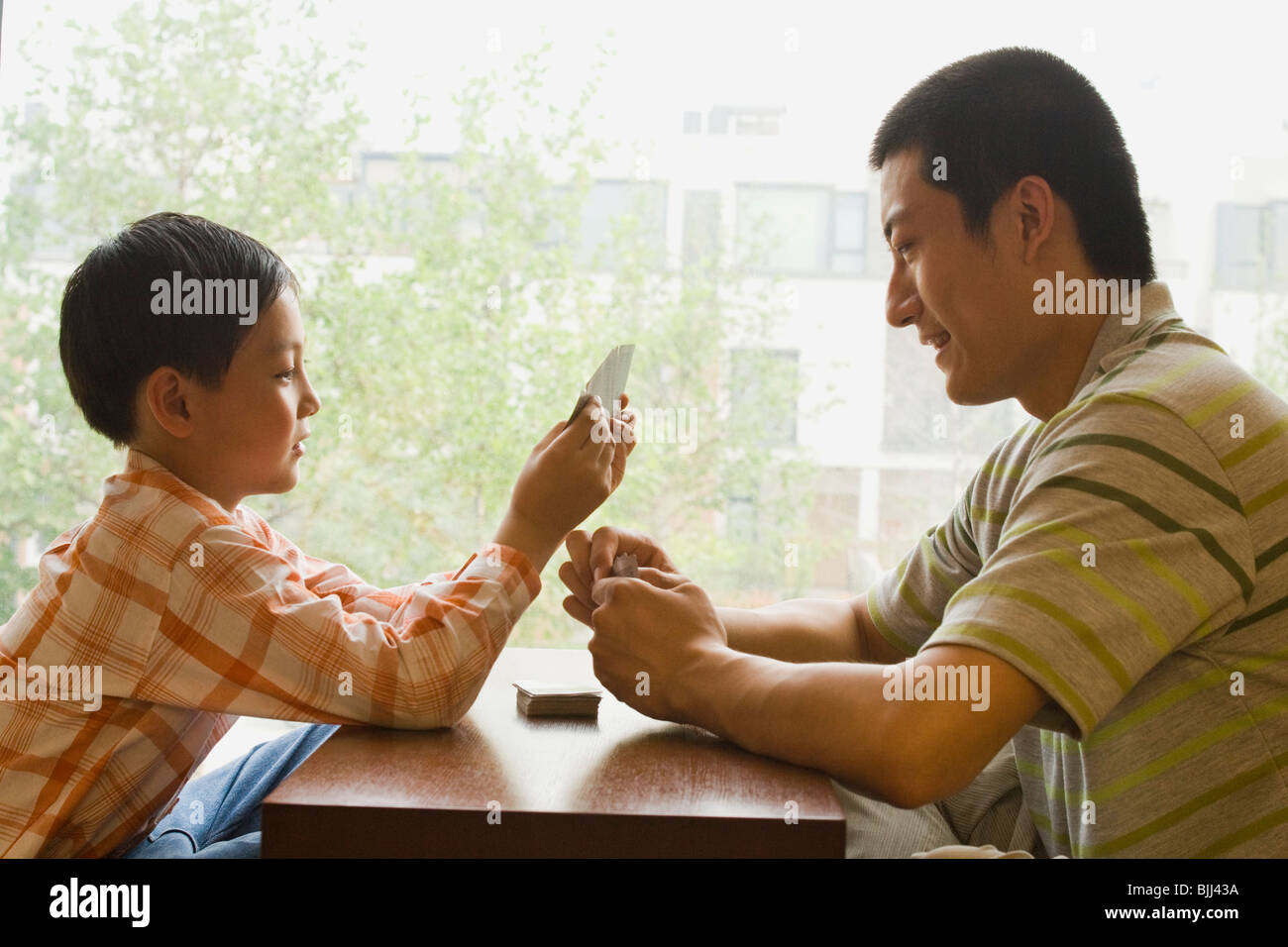 Profile of man and boy sitting cross legged in front of large window playing cards Stock Photo