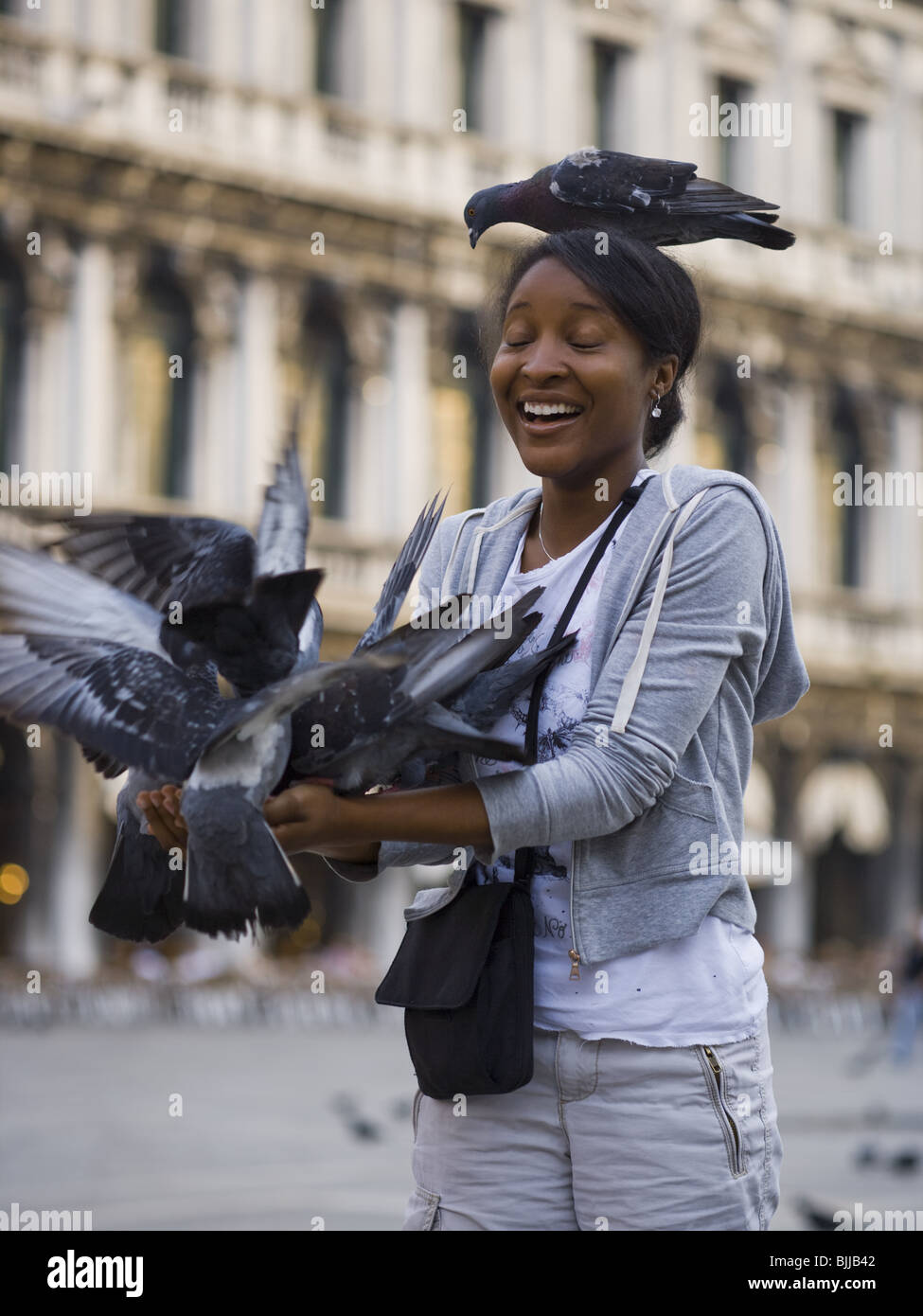 Woman in square with pigeon on head smiling Stock Photo