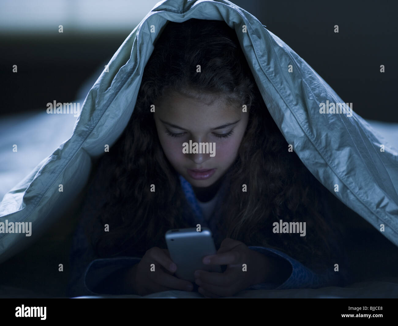 Girl under blankets at night with a smart phone Stock Photo Alamy