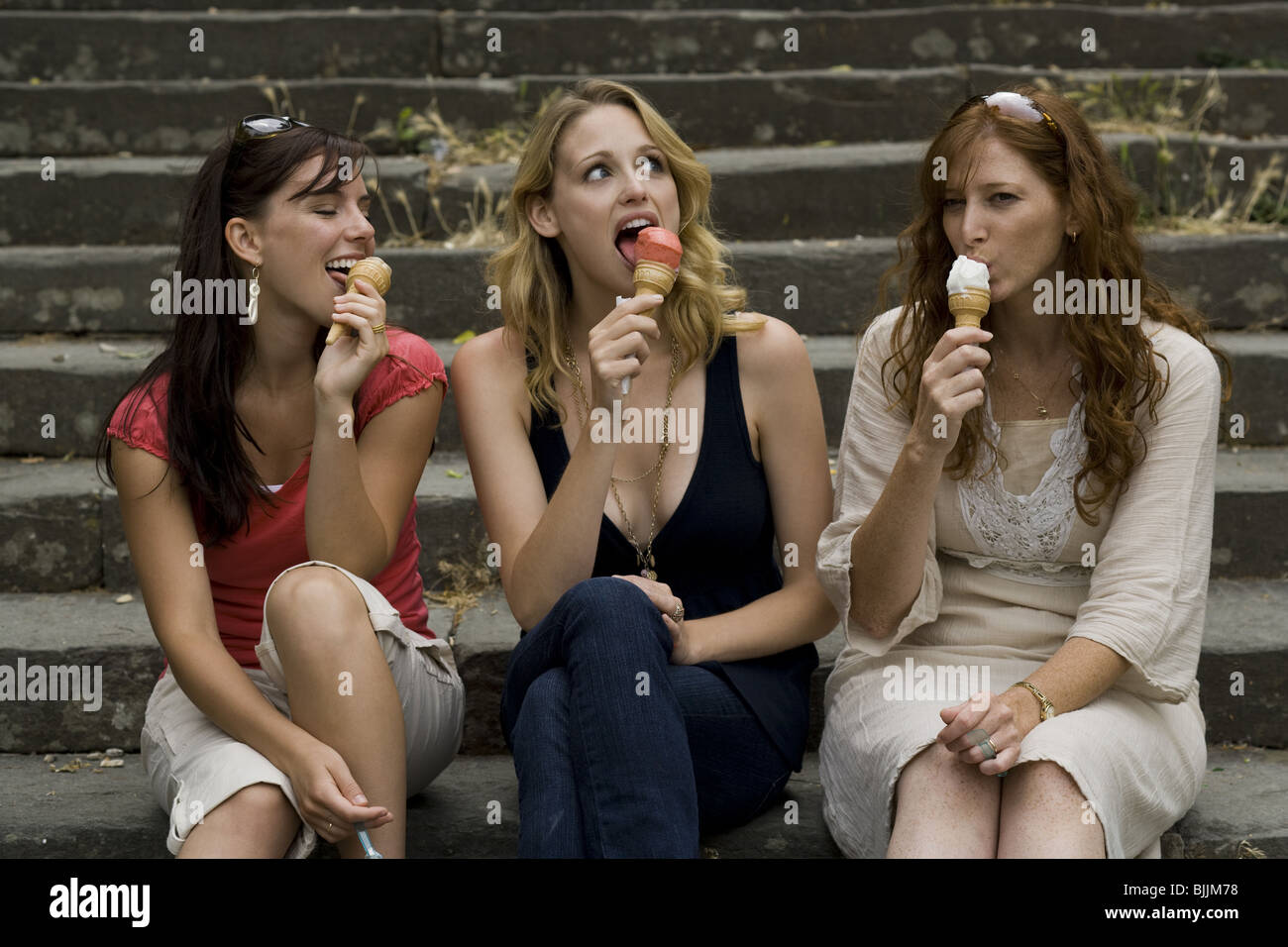 Three women sitting on steps outdoors eating ice cream cones smiling