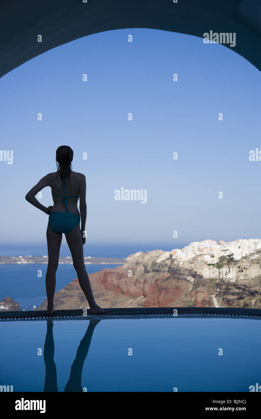 Woman in swimsuit standing at edge of infinity pool rear view Stock Photo