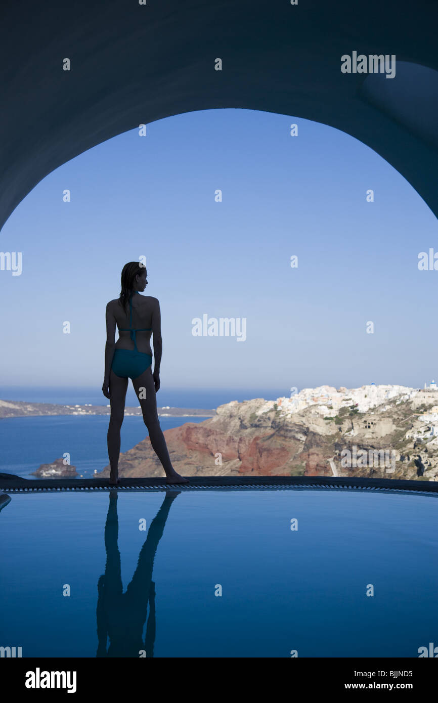 Woman in swimsuit standing at edge of infinity pool rear view Stock Photo