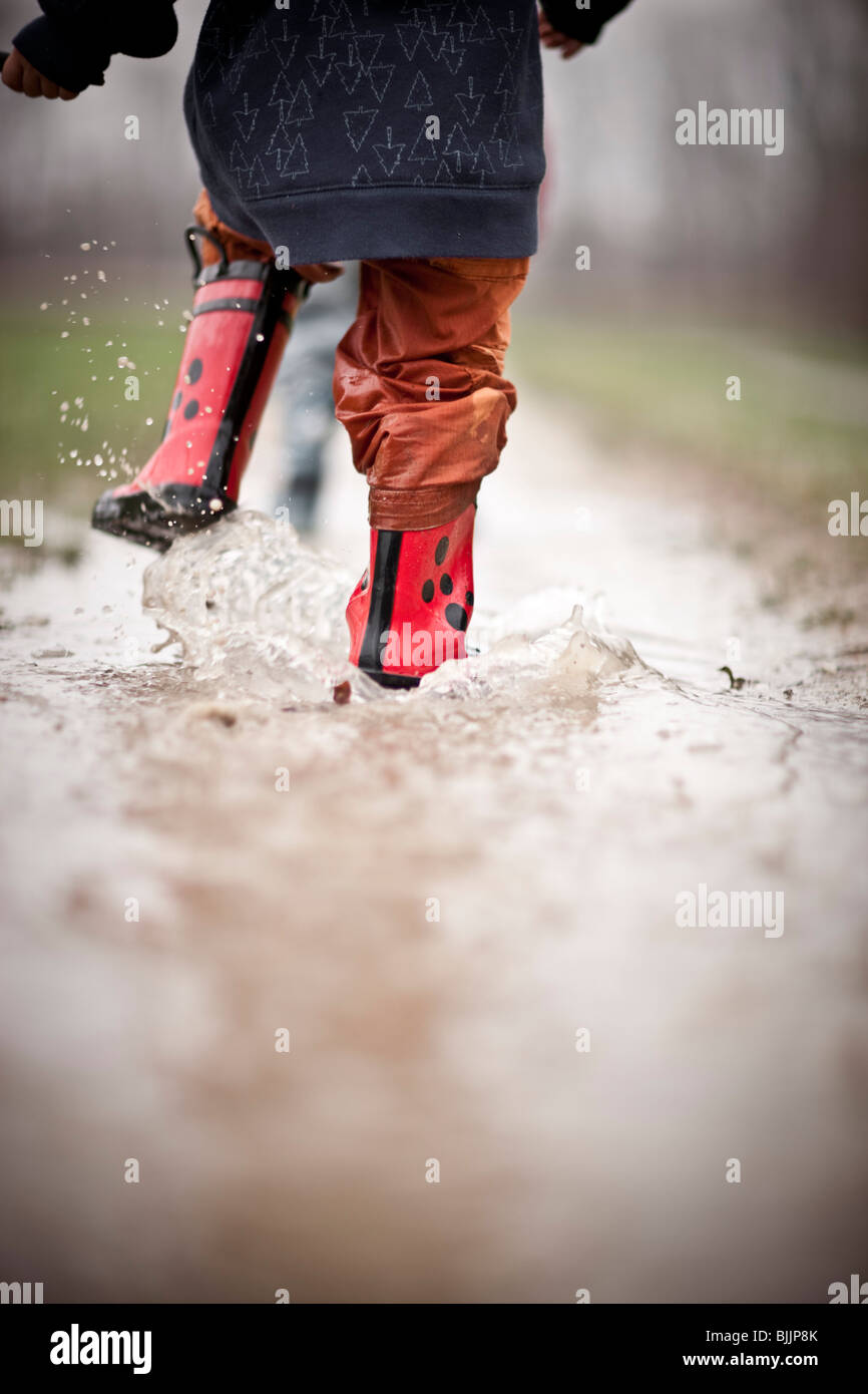 Young boy wearing rain boots walks through a puddle of water. Stock Photo