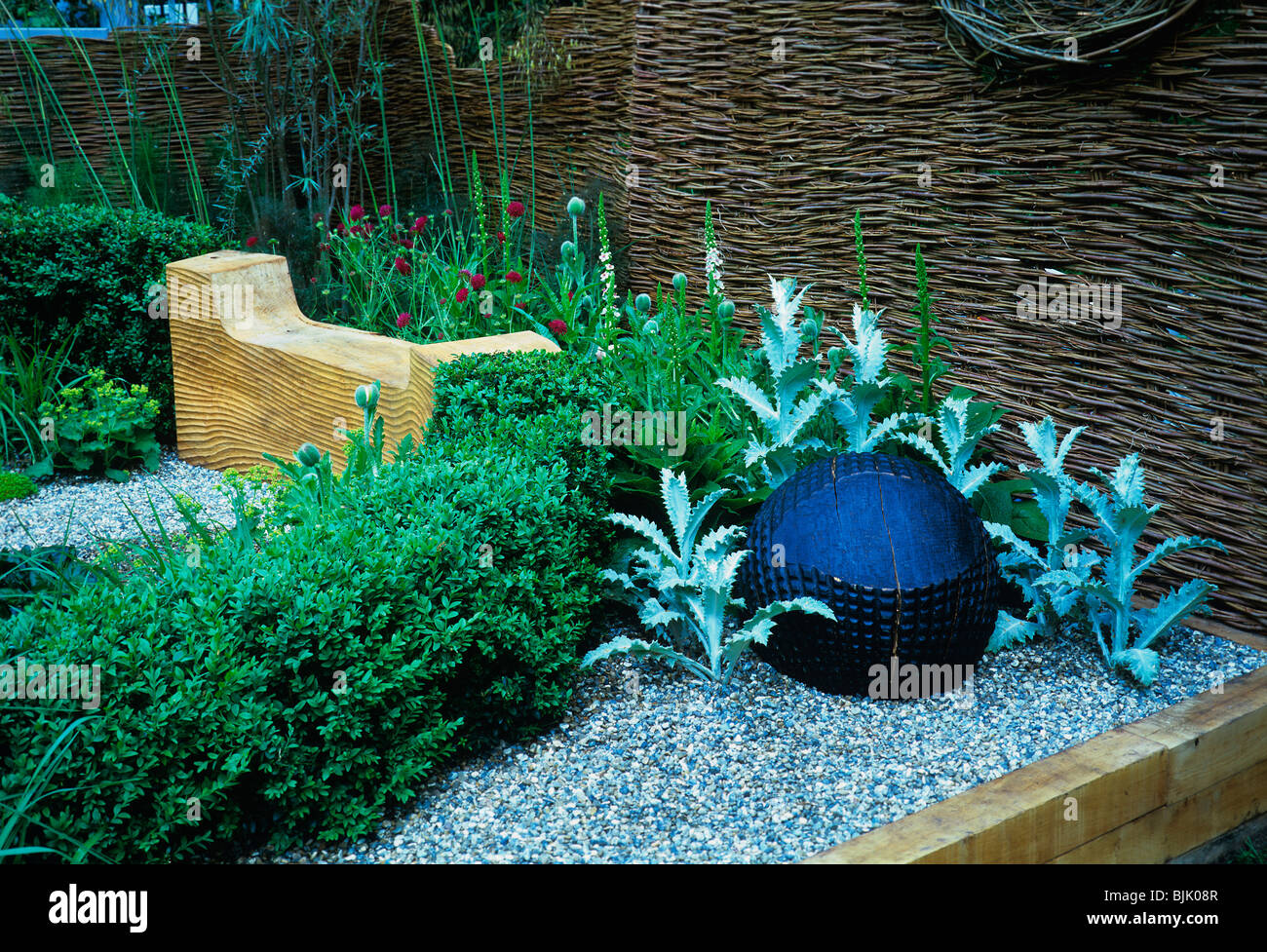 A corner of a small urban garden with decorative carved wooden seat and ball Stock Photo