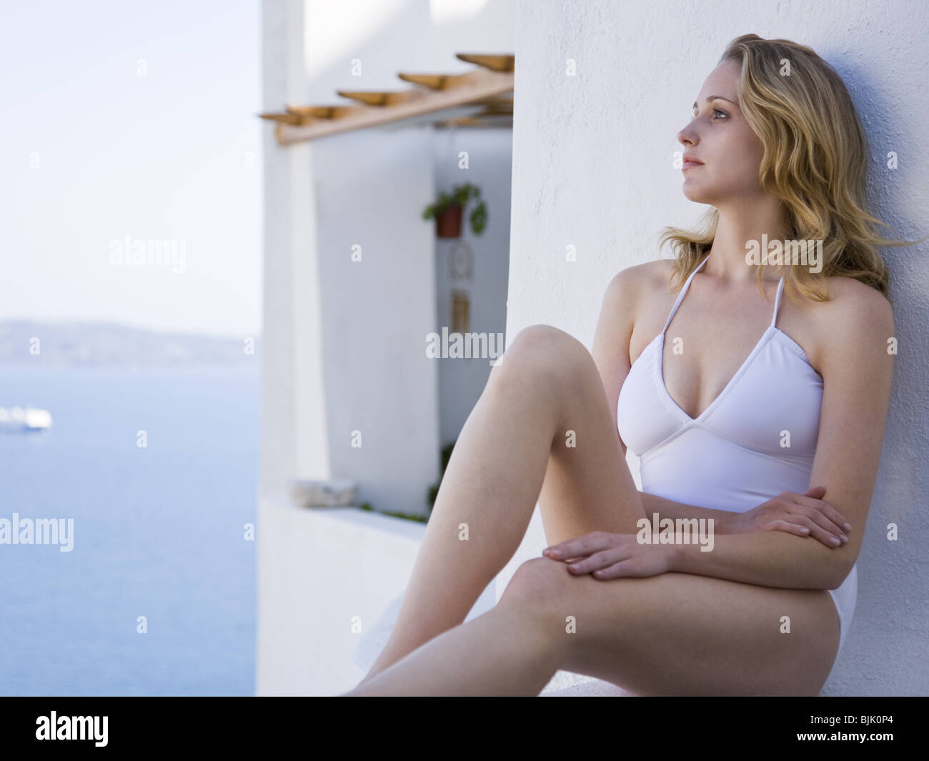 Woman in swimsuit sitting and leaning on wall outdoors smiling Stock Photo