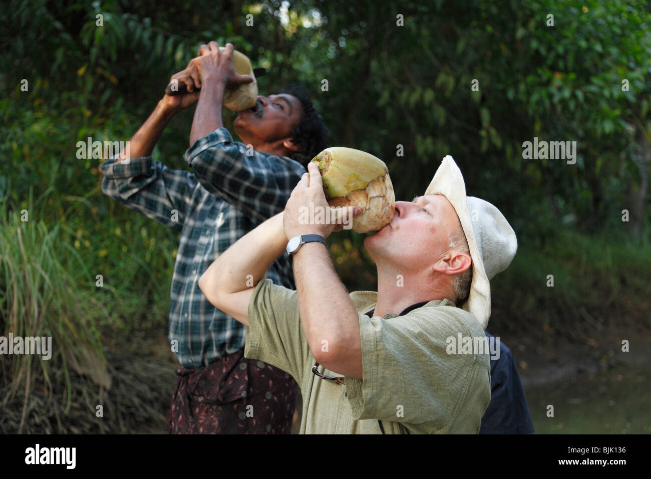 Tourist and an Indian man drinking from a coconut, Kerala, South India, India, Asia Stock Photo