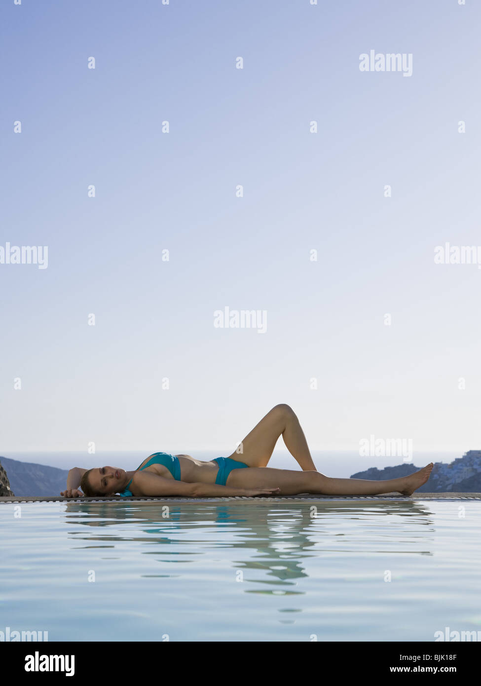 Woman in swimsuit reclining at edge of infinity pool outdoors Stock Photo