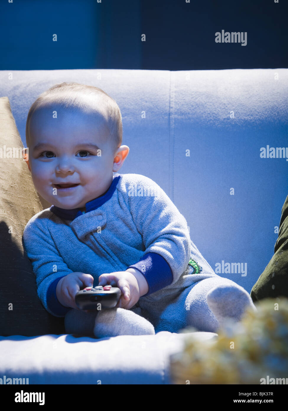 Baby on sofa with television remote smiling Stock Photo
