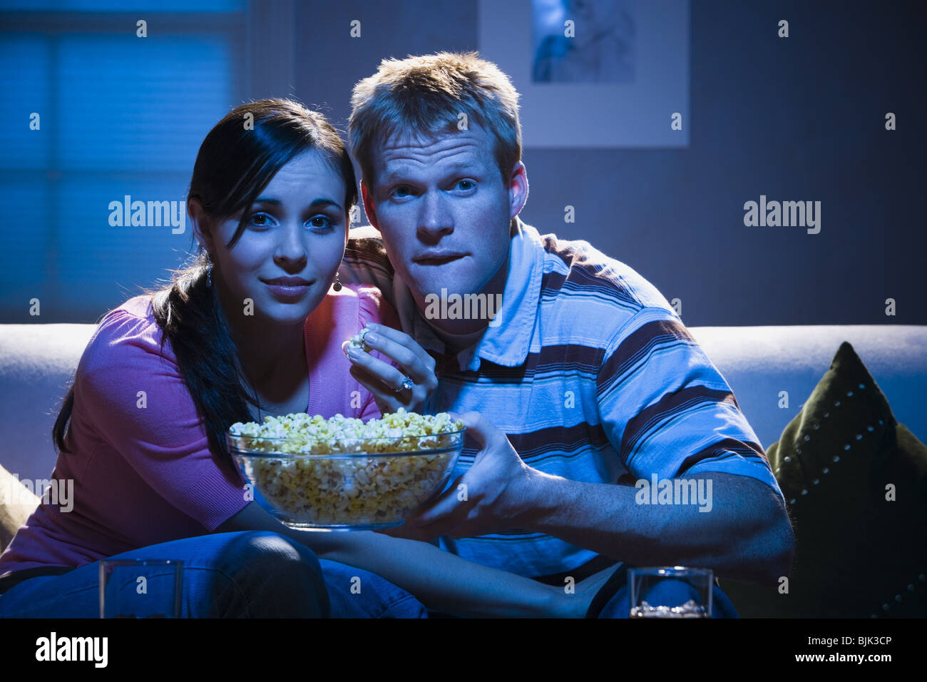 Couple on sofa with bowl of popcorn looking shocked Stock Photo