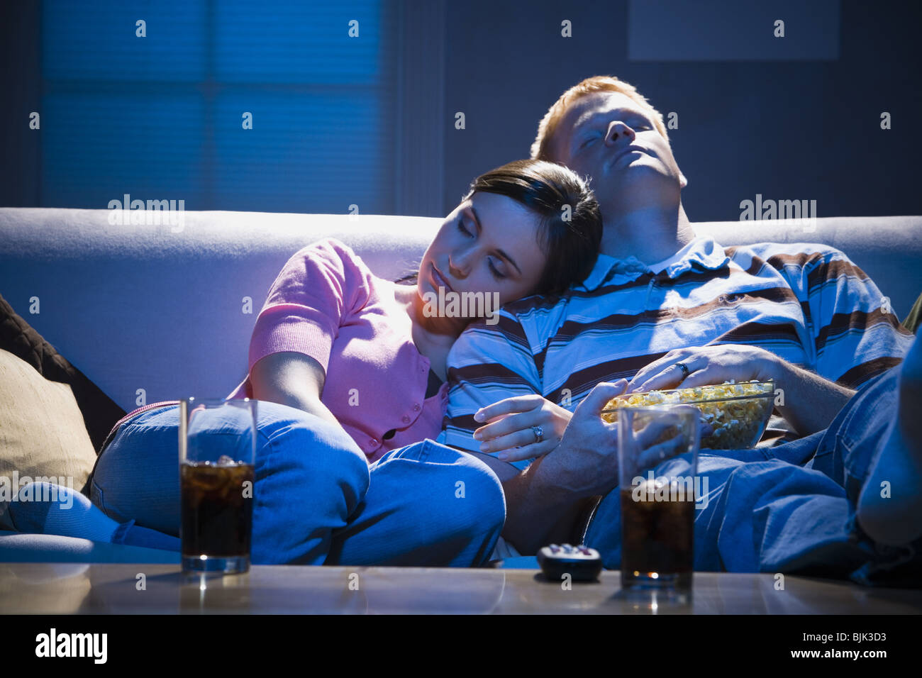 Couple asleep on sofa with bowl of popcorn Stock Photo