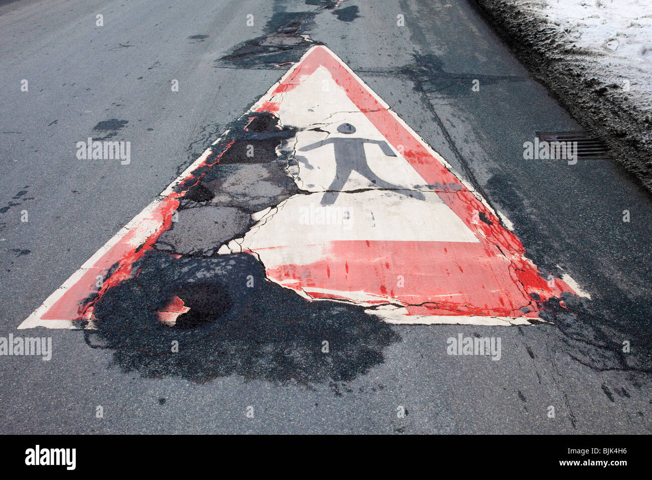 Asphalt cracked by frost and cold with a painted pedestrian crossing sign Stock Photo