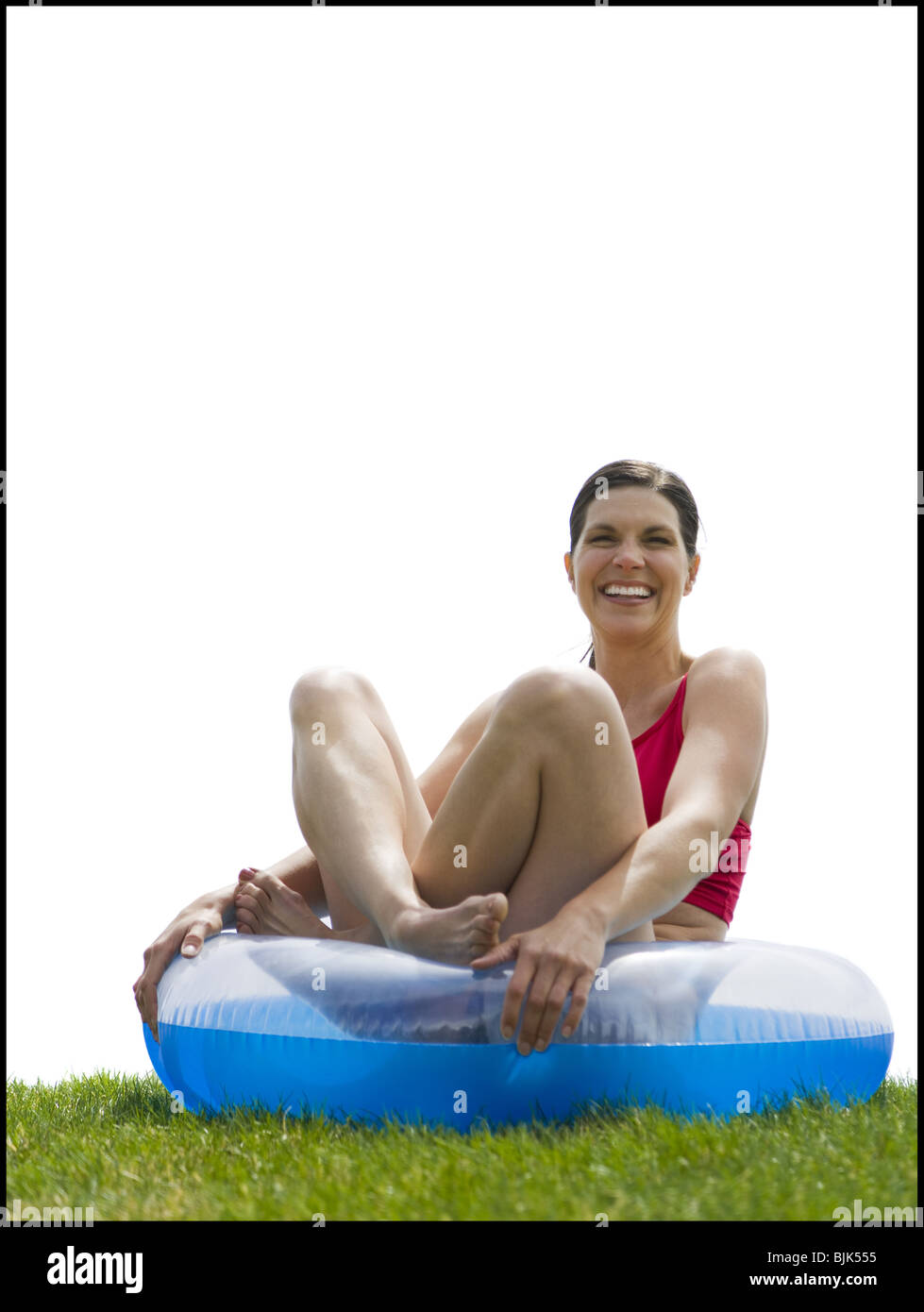 Woman sitting cross legged in swimming ring on grass laughing Stock Photo