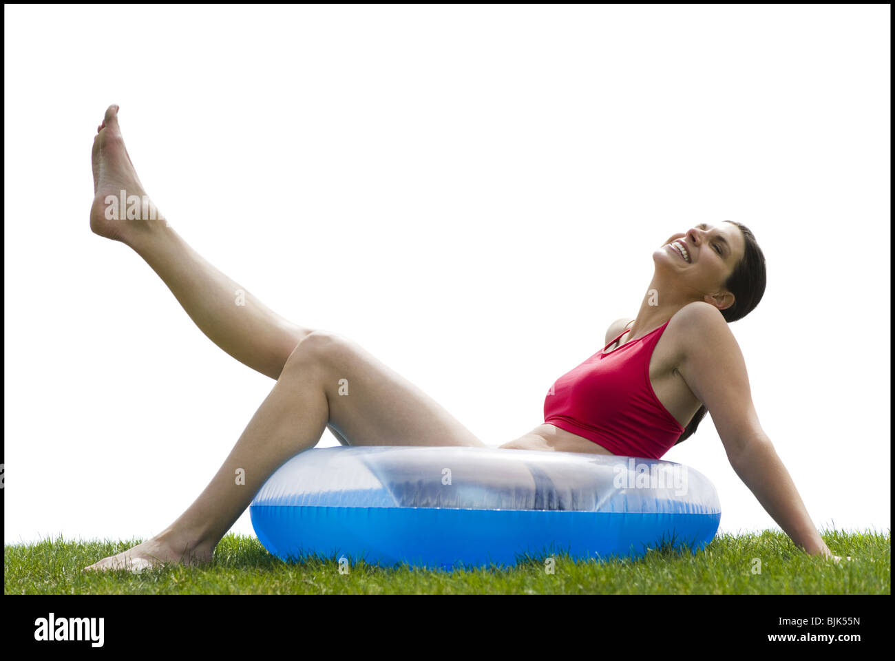Woman sitting in swimming ring on grass with leg up smiling Stock Photo