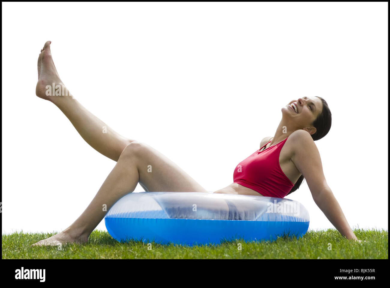 Woman sitting in swimming ring on grass with leg up smiling Stock Photo