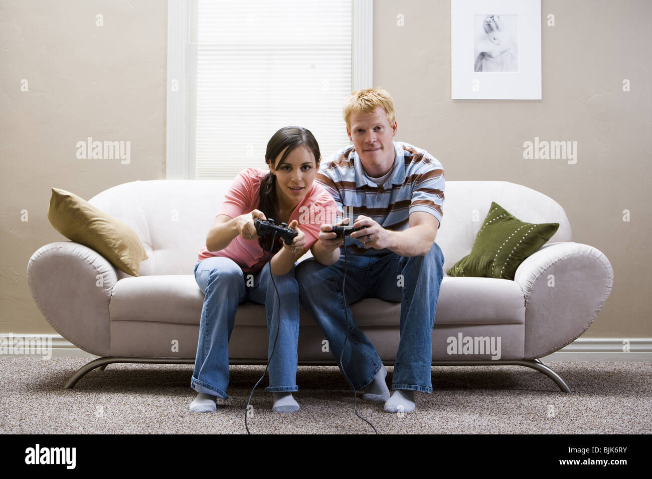 Man and woman sitting on sofa playing video games laughing Stock Photo