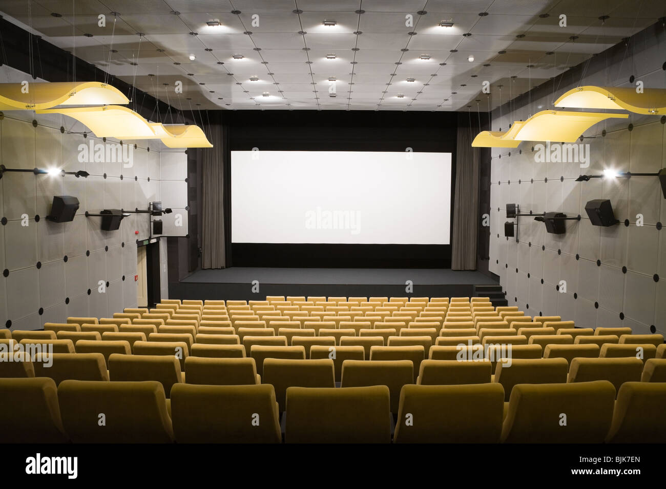 Empty cinema auditorium with line of yellow chairs, stage and projection screen. Ready for adding your own picture. Stock Photo