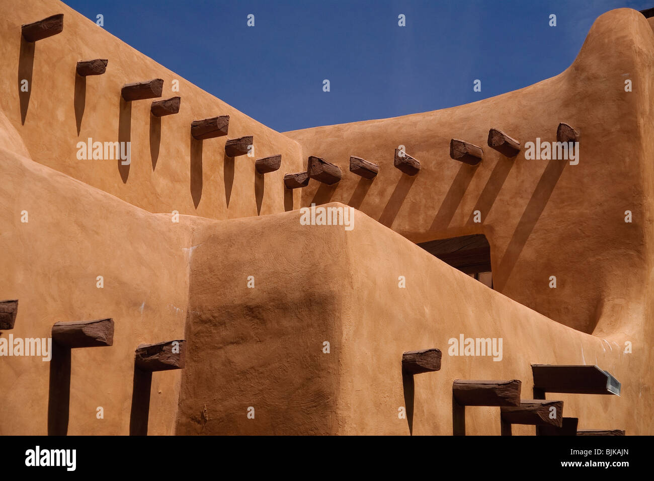 Detail view of the adobe walls of the Santa Fe Museum of Fine Arts, with exposed wooden beams, contrasting against the blue sky Stock Photo