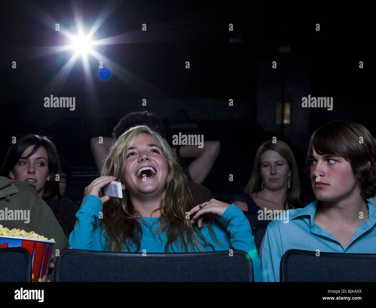 Girl talking on cell phone at movie theater with annoyed boy Stock Photo