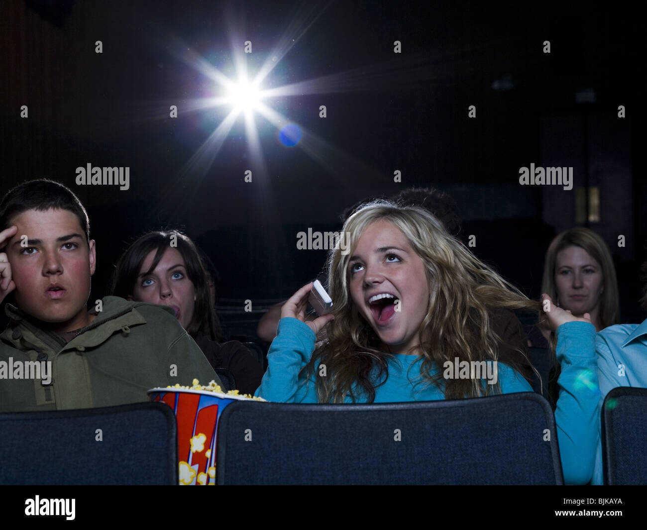 Girl talking on cell phone at movie theater with annoyed boy Stock Photo