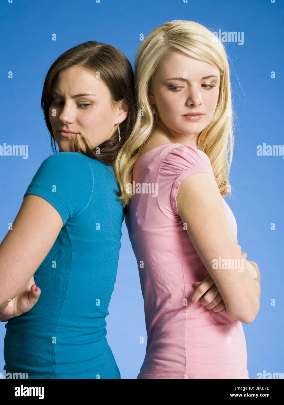 Two girls with arms crossed back to back scowling Stock Photo Alamy