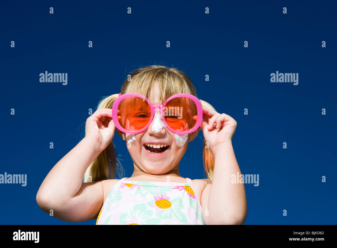 Girl with suntan lotion and sunglasses smiling with arms up Stock Photo