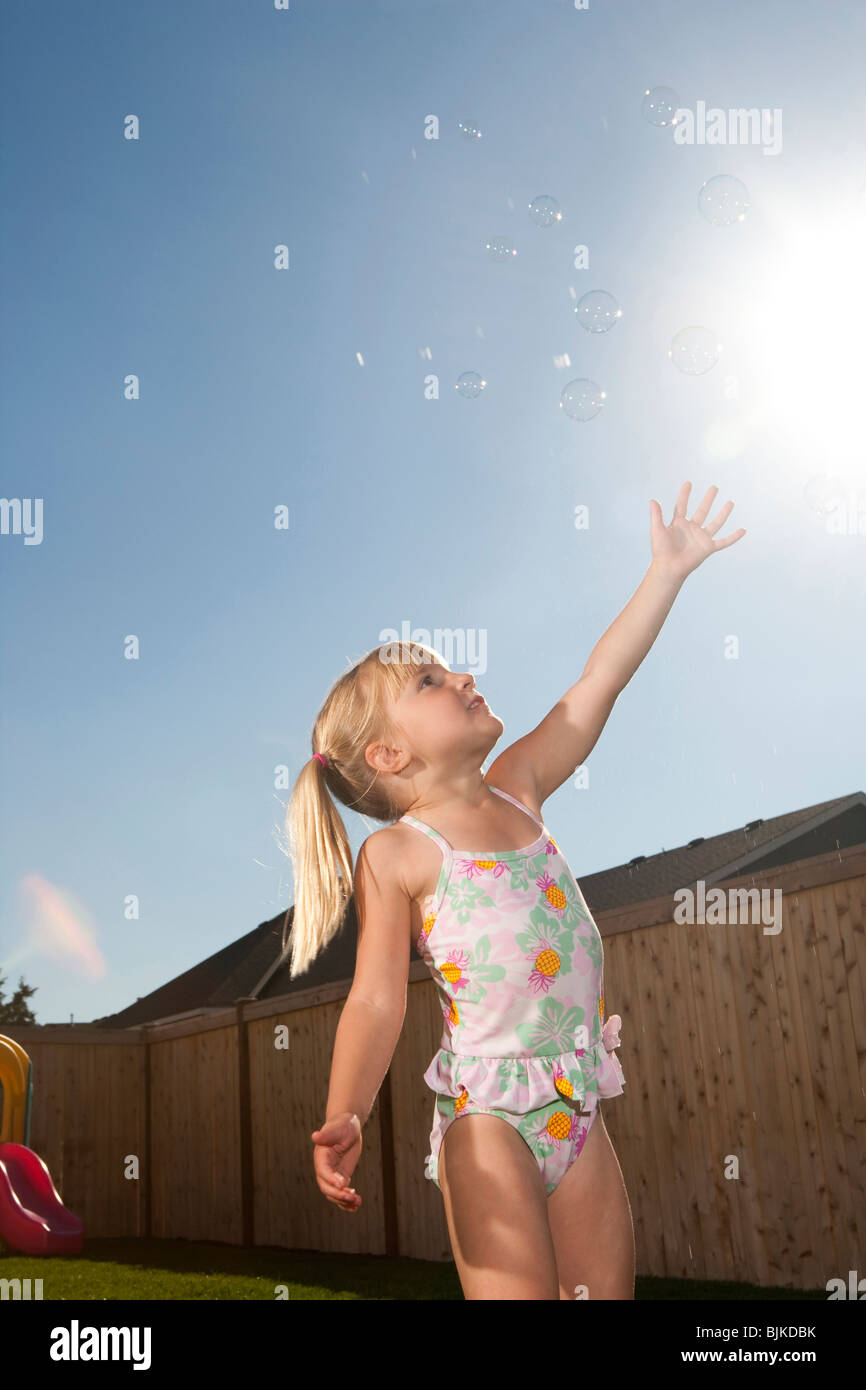 Girl in swimsuit catching bubbles outdoors with blue sky Stock Photo