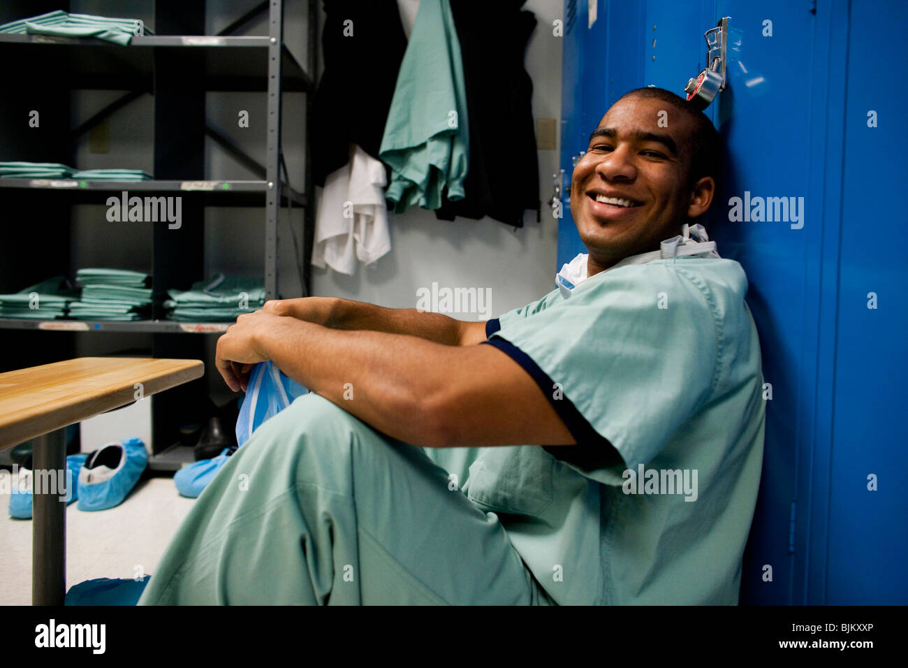 Male doctor in scrubs sitting in locker room Stock Photo