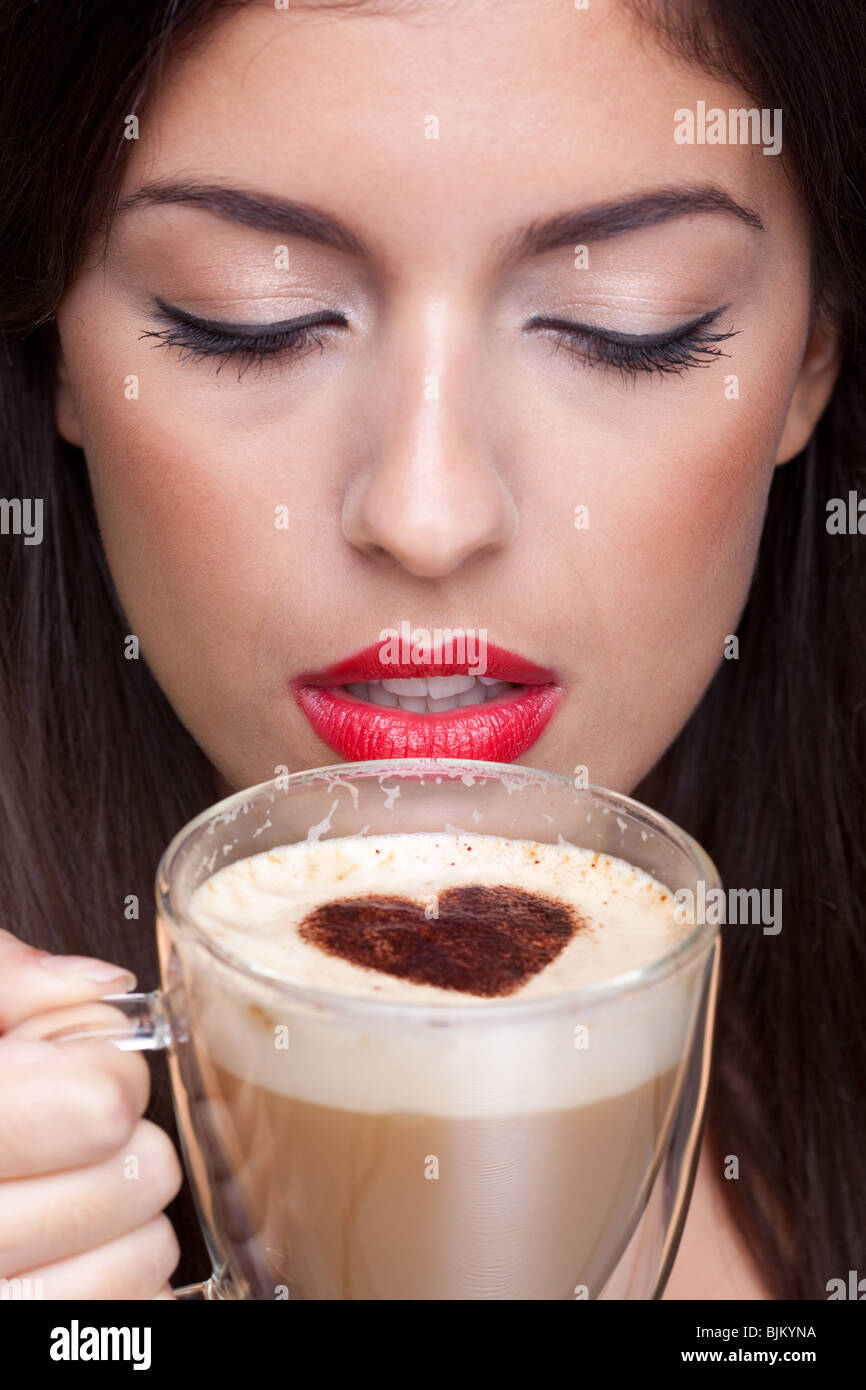 Woman drinking a cappuccino coffee with a love heart shape sprinking on top. Stock Photo
