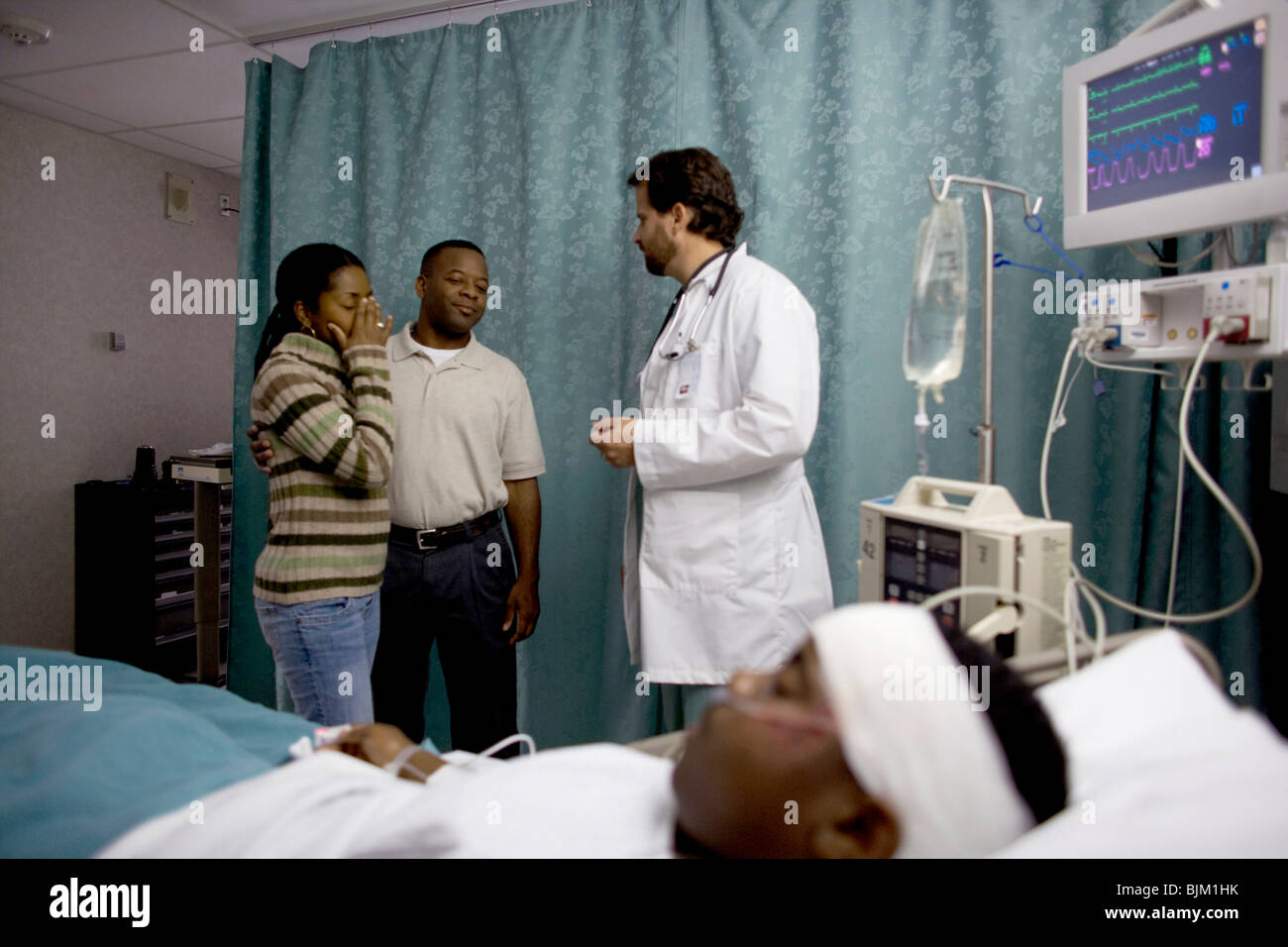 Parents of boy in hospital bed talking to doctor Stock Photo