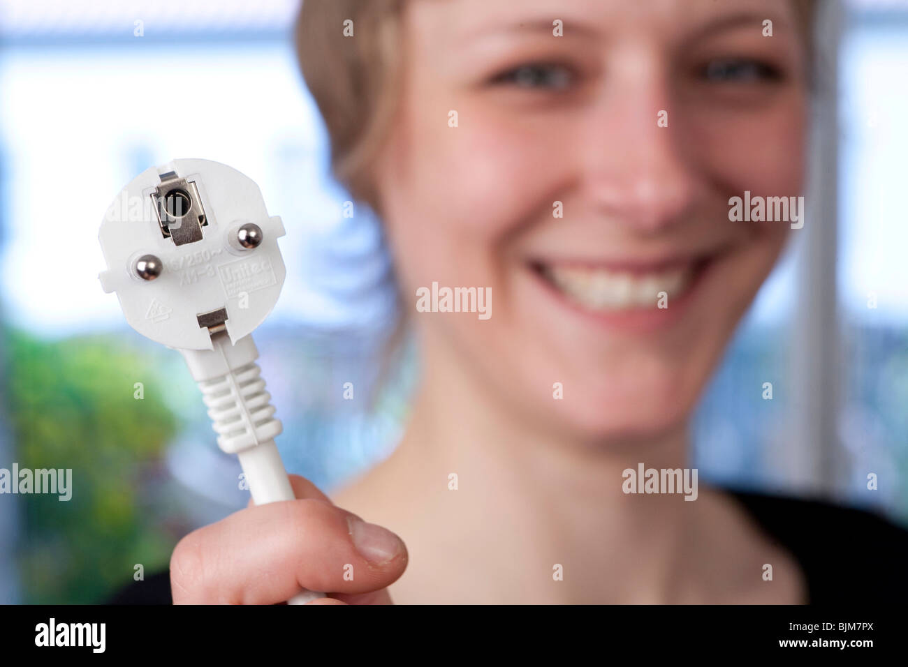 Smiling young woman holding a power plug in her hand Stock Photo