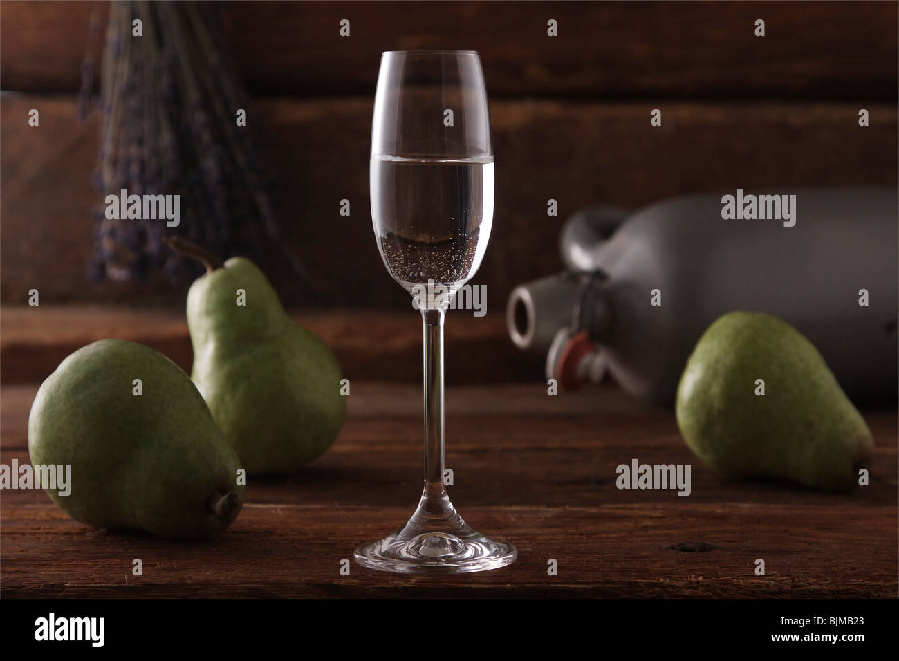 Glass of pear brandy with pears and a whiskey jar on a rustic wooden background Stock Photo