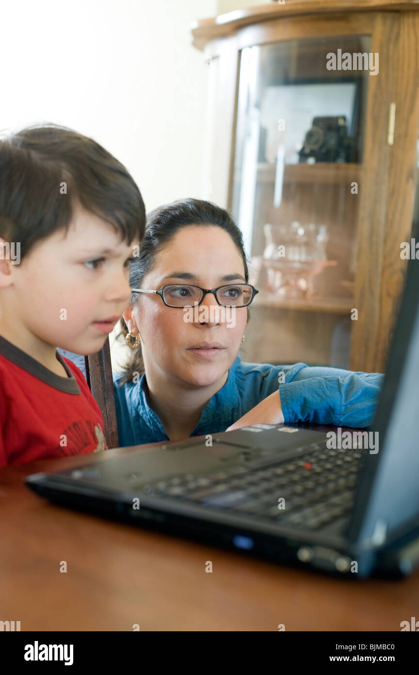 Four and 1/2 year old Hispanic boy surfs the internet on his laptop at home with the help of his mother. Model Released. Stock Photo