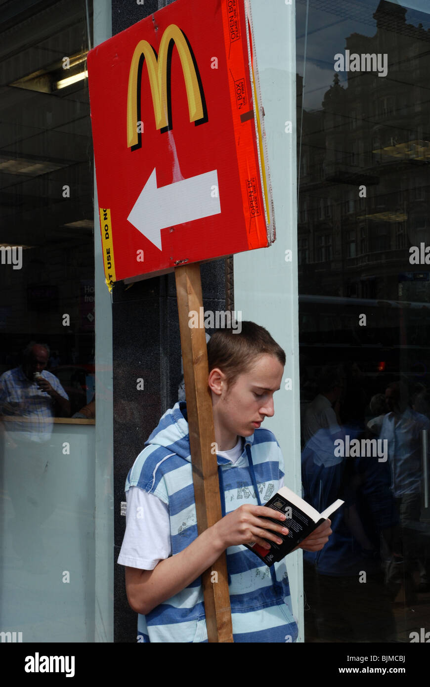 A youth reads whilst holding a sign pointing towards a McDonald's Stock Photo