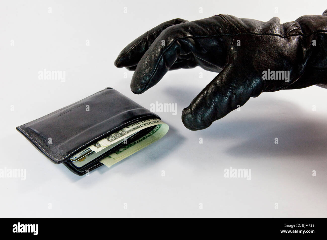 Thief, fraudster, glove reaching for a wallet with cash and credit cards Stock Photo