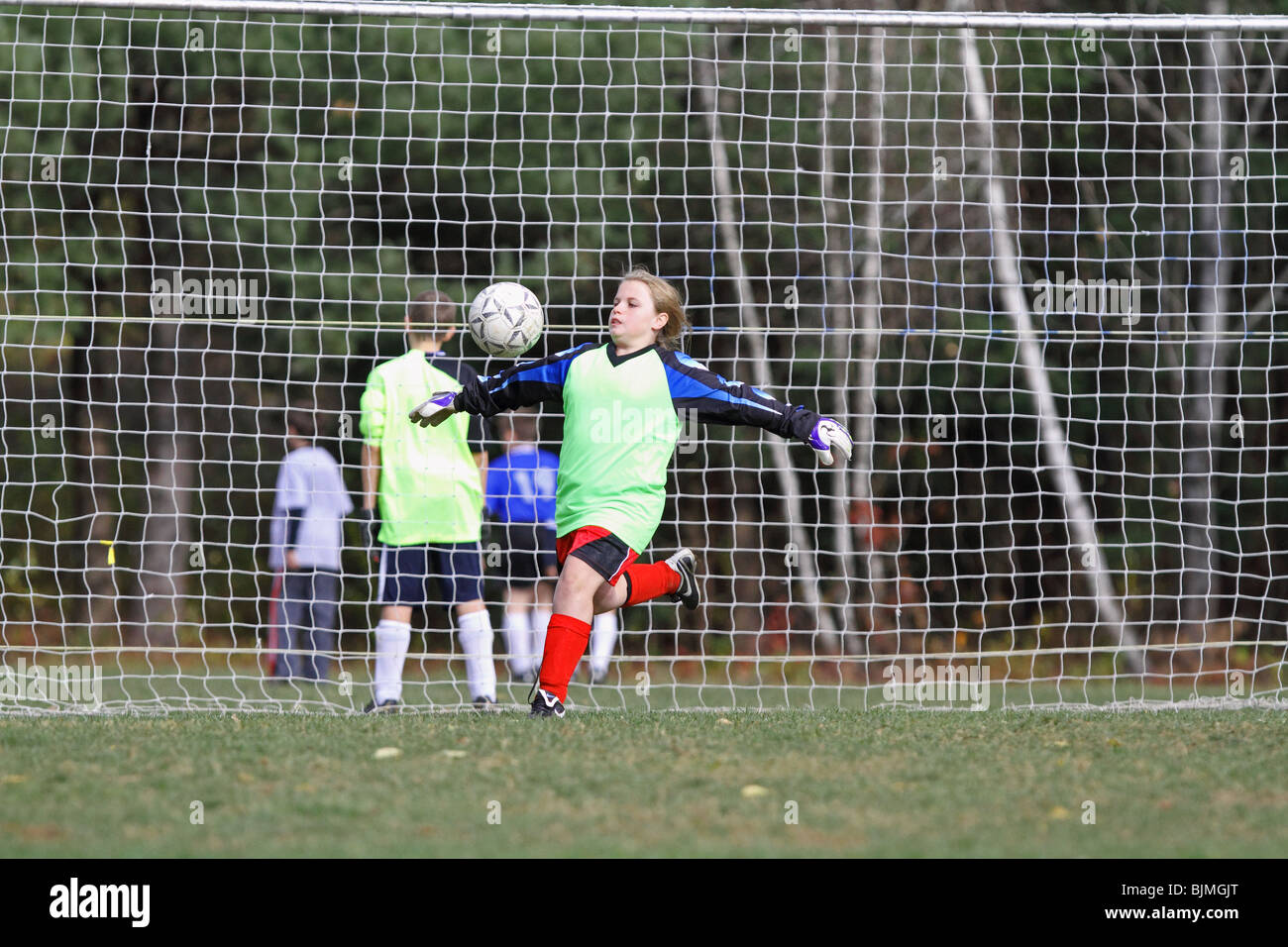Caucasian female soccer player goalie kicks ball midair Stock Photo
