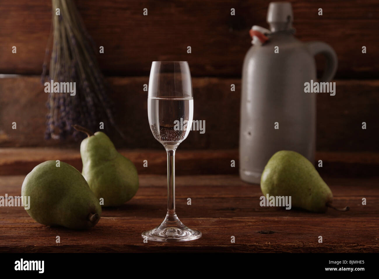 Glass of pear brandy with pears and a whiskey jar on a rustic wooden background Stock Photo