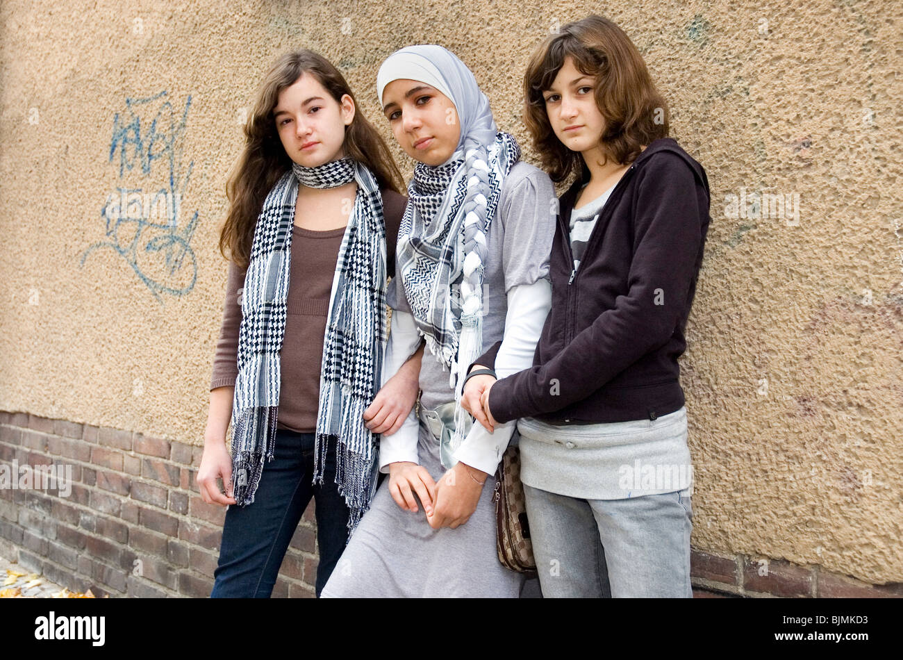 Three girls leaning on a house wall, Berlin, Germany Stock Photo