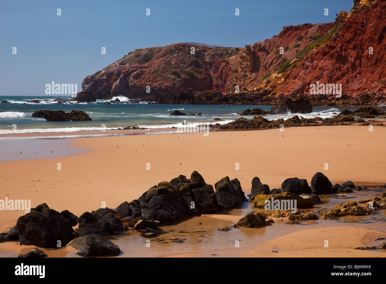 Rocks in the sea and on the beach with red cliffs and blue sky in