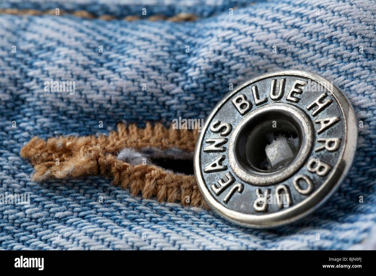 Close up image of the metal waist band fastening on a pair of faded blue denim jeans showing the makers brand name Stock Photo