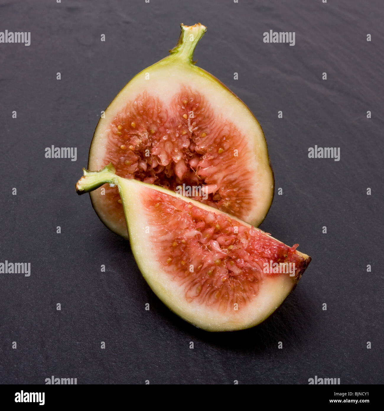 Sliced ripe figs from low viewpoint isolated against dark slate background. Stock Photo