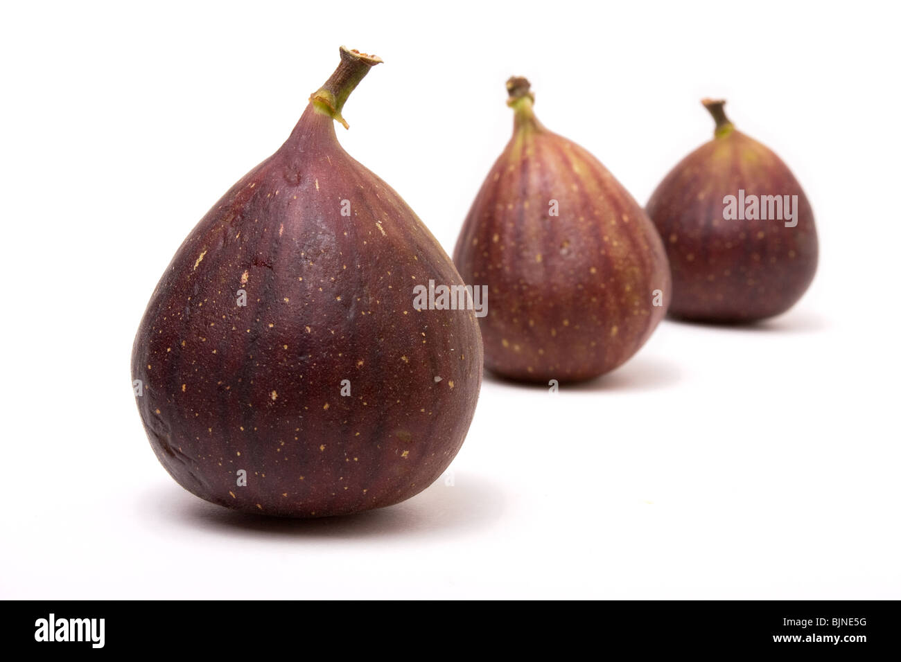 Abstract arrangement of Three ripe figs isolated against white background. Stock Photo